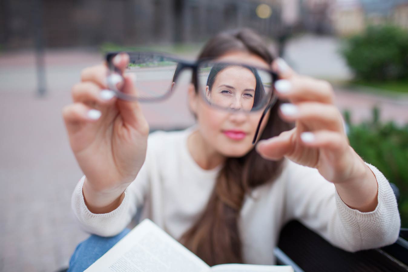 A woman holding glasses that make her face appear smaller through the lens